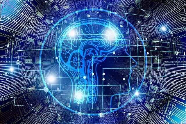 Ein stilisiertes blaues Bild eines menschlichen Kopfprofils mit einem leuchtenden Gehirn im Inneren, umgeben von konzentrischen Kreisen und einem komplexen Netzwerk aus digitalen Schaltkreisen, das Künstliche Intelligenz und Technologie symbolisiert.